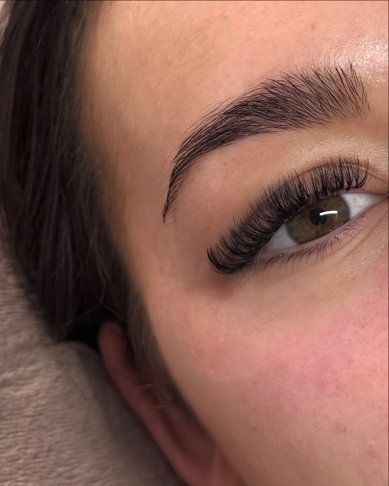 Close-up of a Russian volume lash set — dark, fanned lashes on a green-hazel eye beneath a groomed brow.